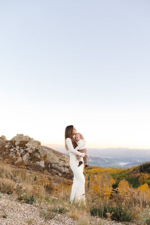 Two people in white clothing dance together on a rocky mountain overlook at sunset.