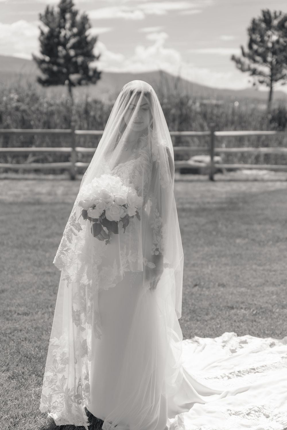 Black and white portrait of veiled bride holding white bouquet in outdoor field setting.