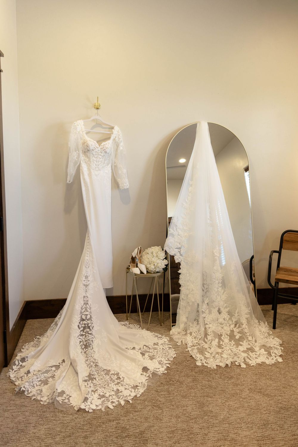 Elegant white lace wedding gown with long train displayed on hanger beside full-length mirror.