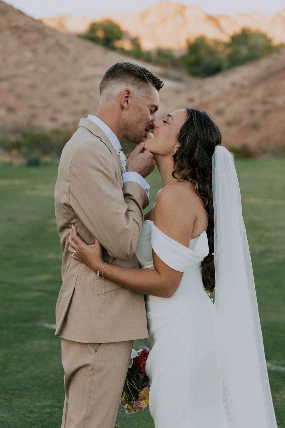 Bride and groom share a romantic kiss in golden hour light with mountain backdrop.