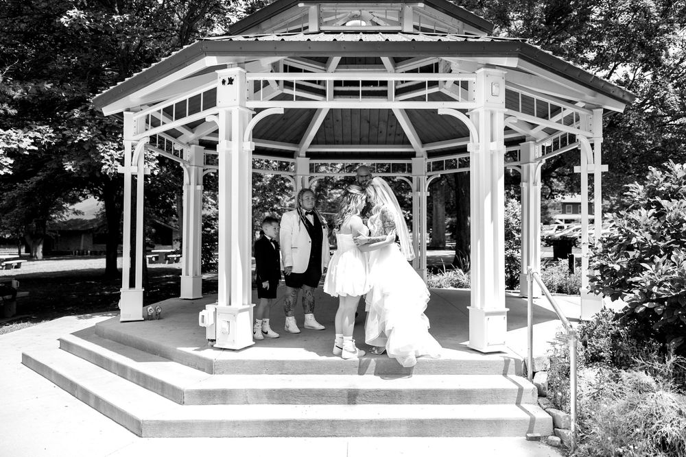 Wedding ceremony at white gazebo with brides, and officiant in black and white photo.