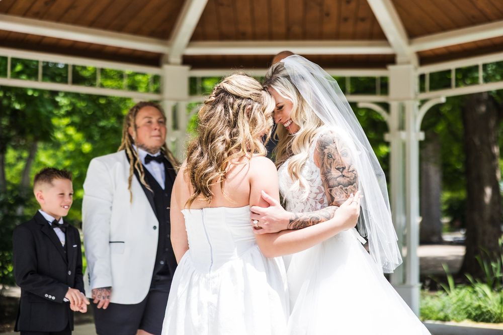 Bride and daughter sharing emotional first look embrace at outdoor gazebo wedding ceremony.