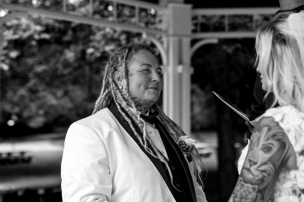 Black and white portrait of bride with dreadlocks in white suit at outdoor wedding ceremony.