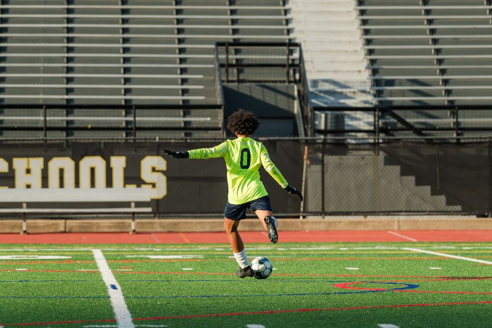 Soccer players perform agility drills on a green turf field with orange cones during training session.