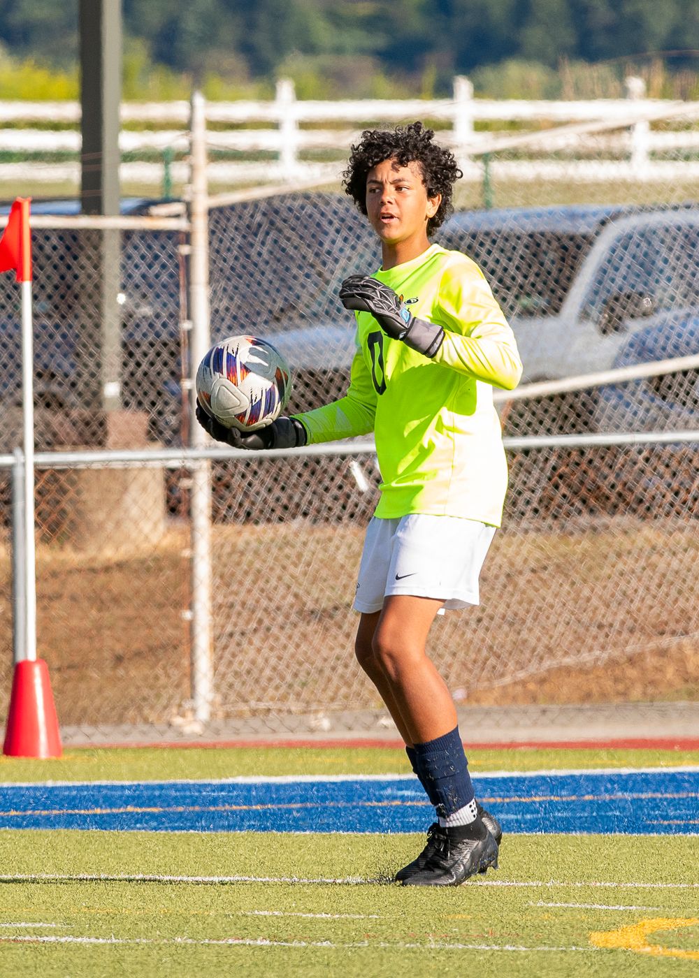 A soccer goalkeeper in bright yellow uniform dives to make a save on a blue turf field during a match.