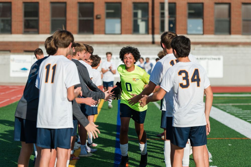 Soccer players in white and yellow jerseys gather on a turf field during a game or practice session.