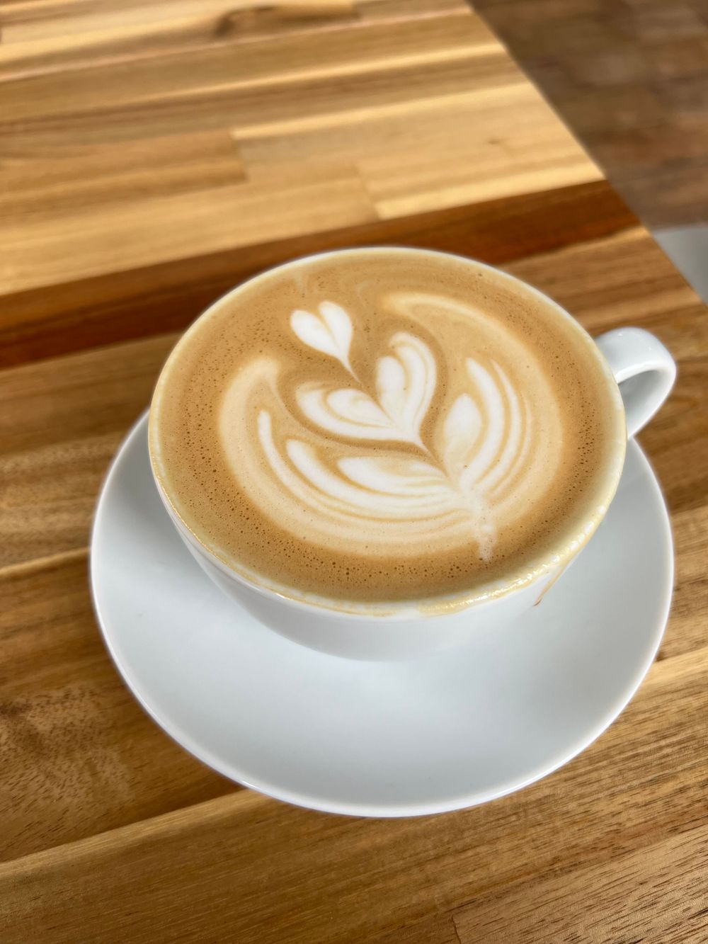 A latte art progression showing multiple stages of creating a heart design in coffee foam on a white cup against a wooden surface.