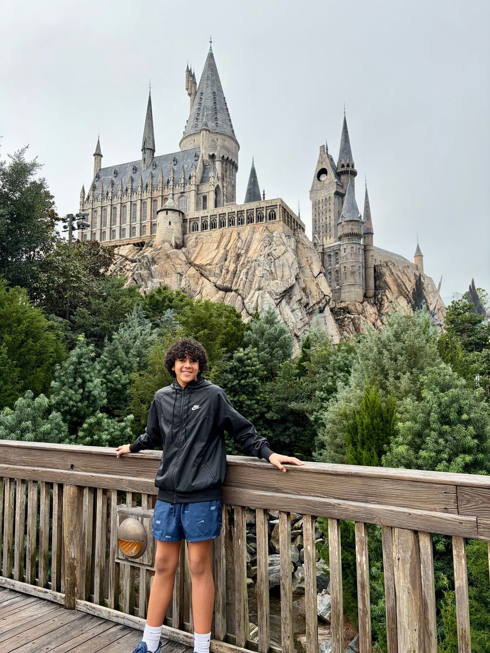 A visitor poses at different spots along a wooden viewing bridge with Hogwarts Castle from Universal Studios in the background.