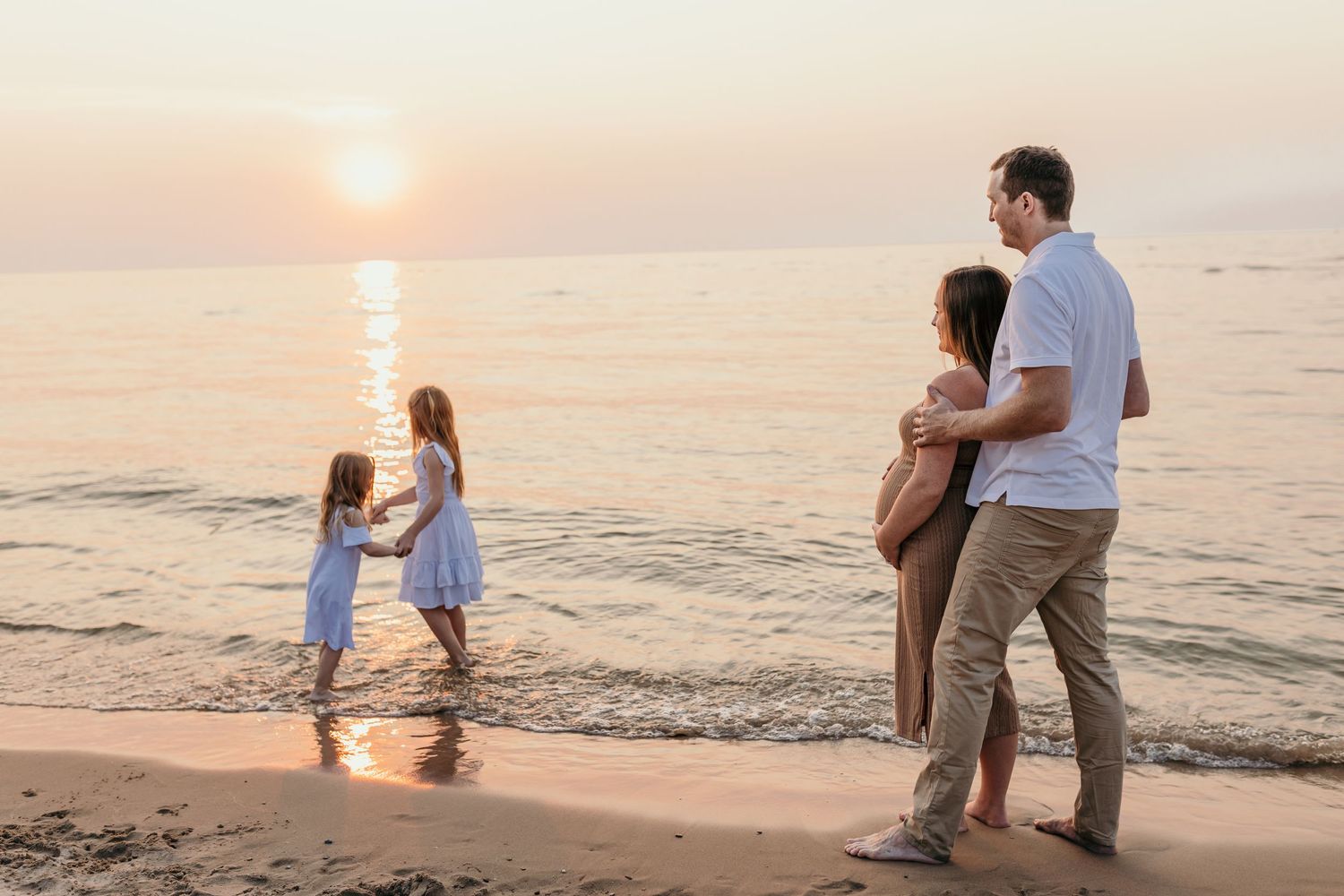 Family enjoying sunset beach walk with child playing in gentle waves.