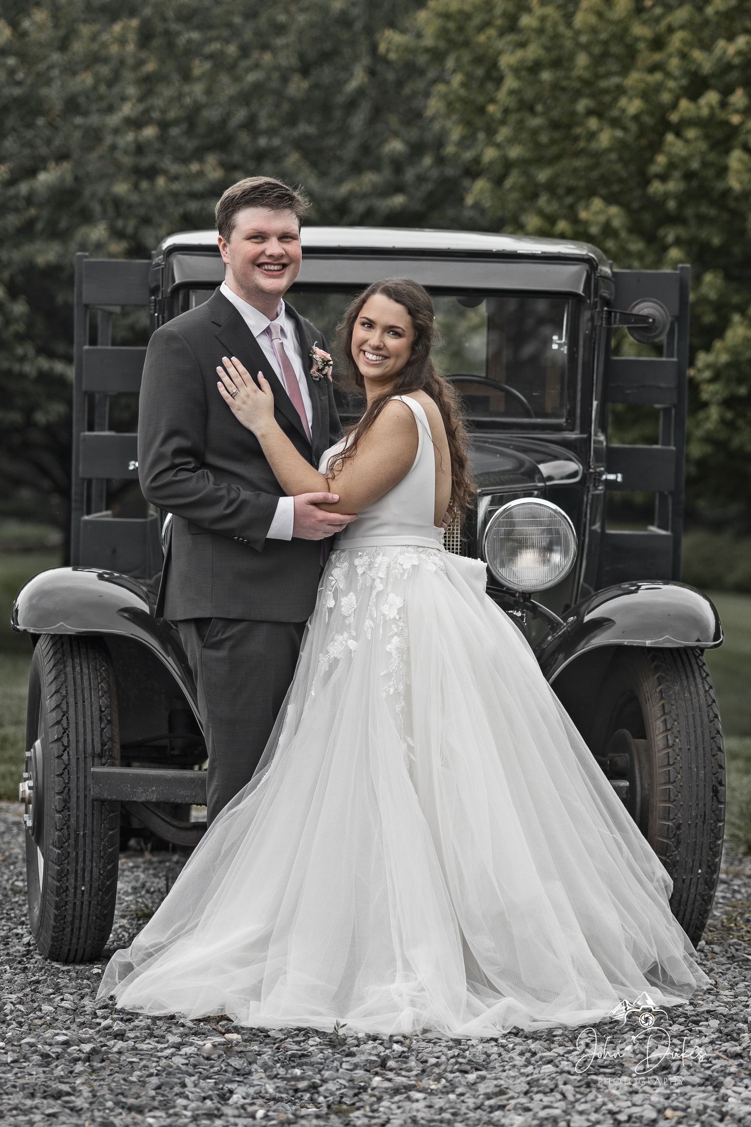 Newlyweds pose with vintage black car for wedding photos.