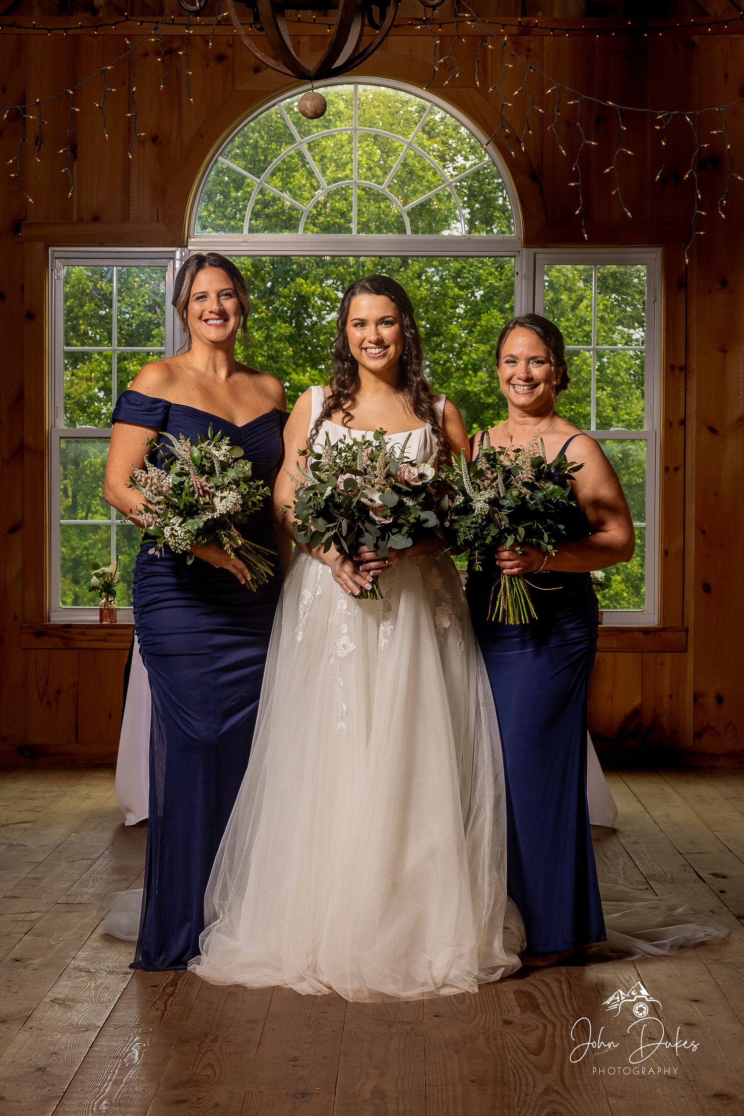 Bridesmaids in navy dresses stand with the bride in a rustic wooden venue.