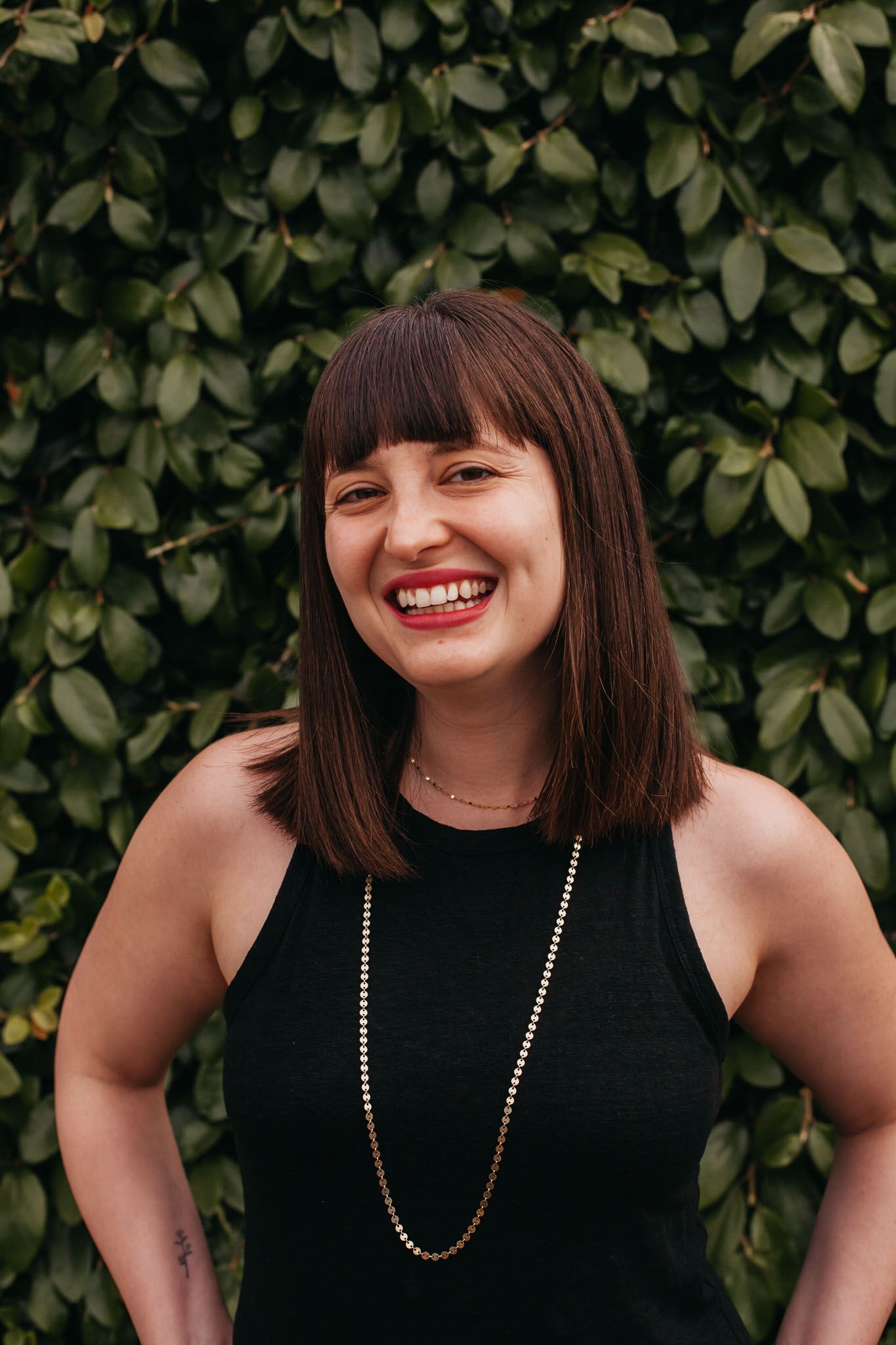 Author Alison Raskin poses in front of a leafy green wall.