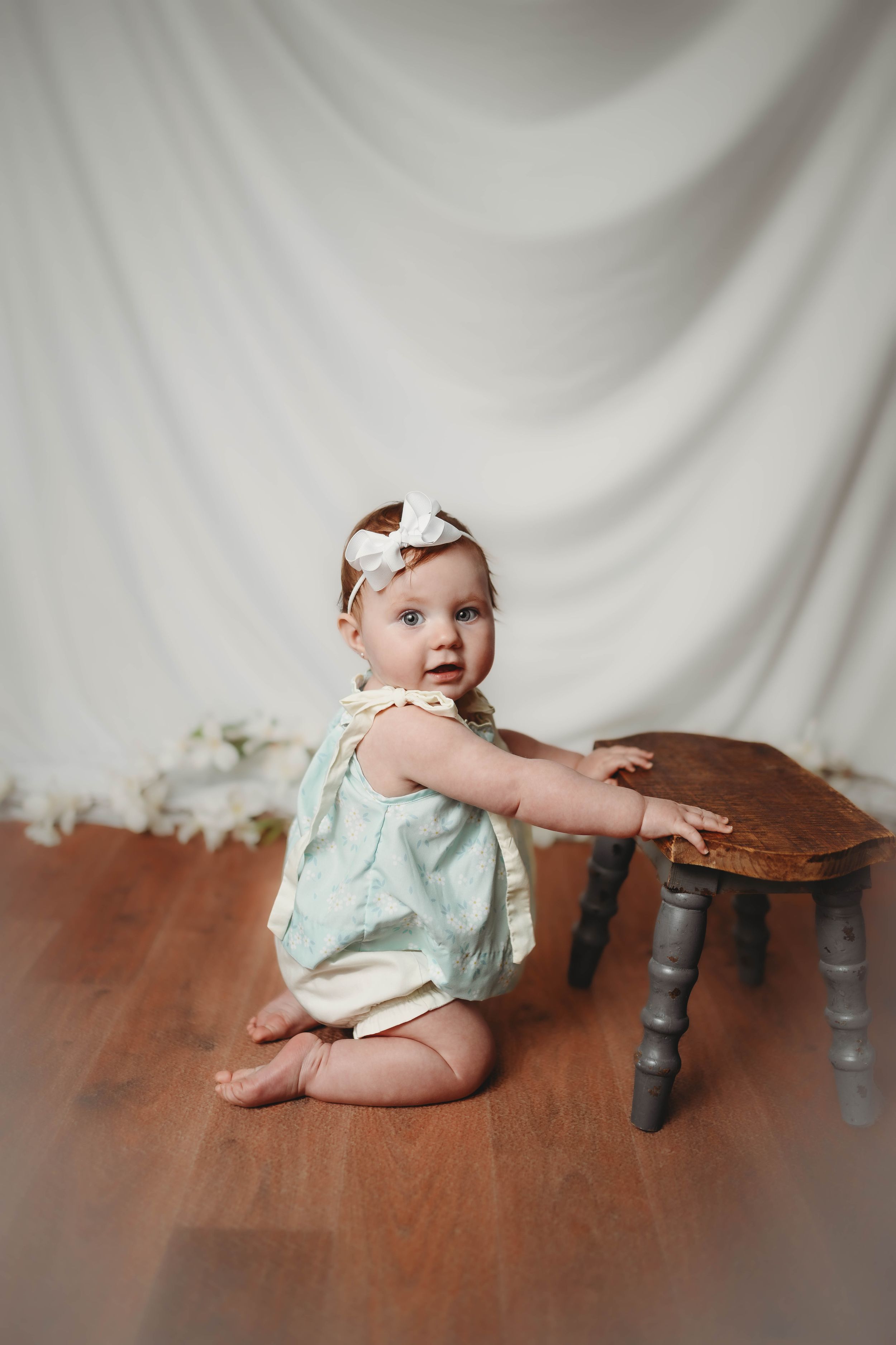 Baby in mint green outfit posing with wooden table against white backdrop.