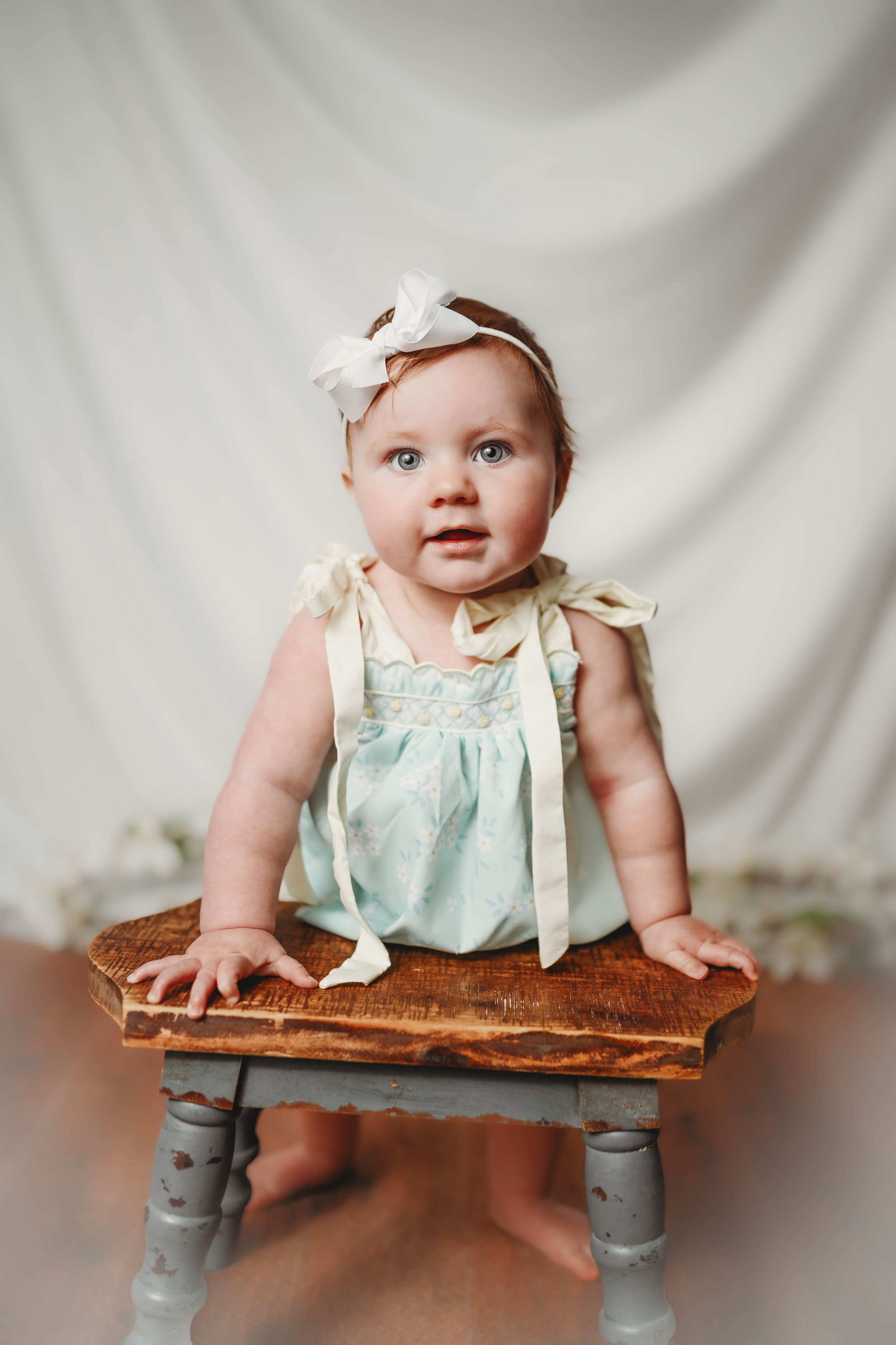Baby in mint dress sitting on rustic wooden table with gray legs.