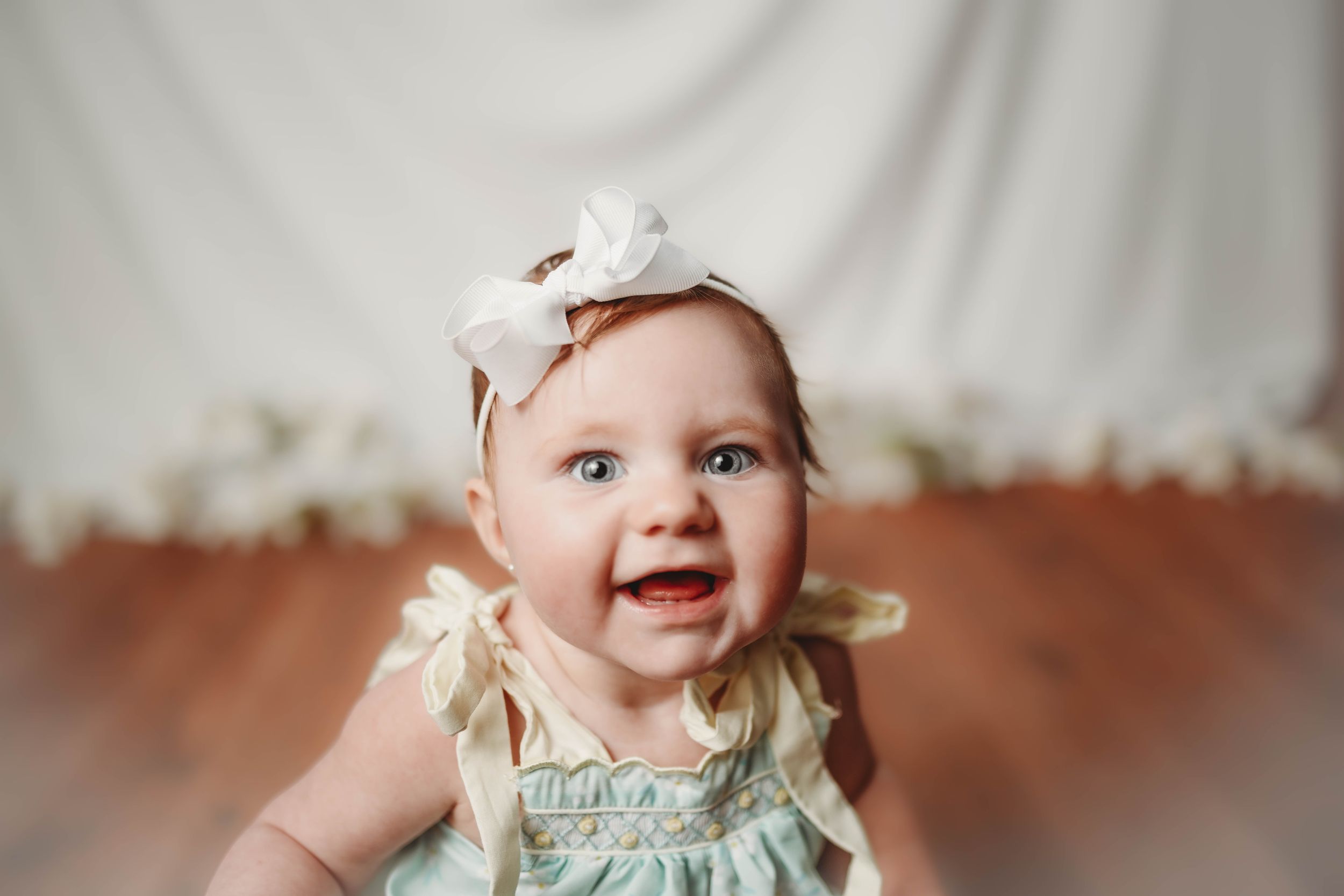 Baby in mint dress smiling against white backdrop.