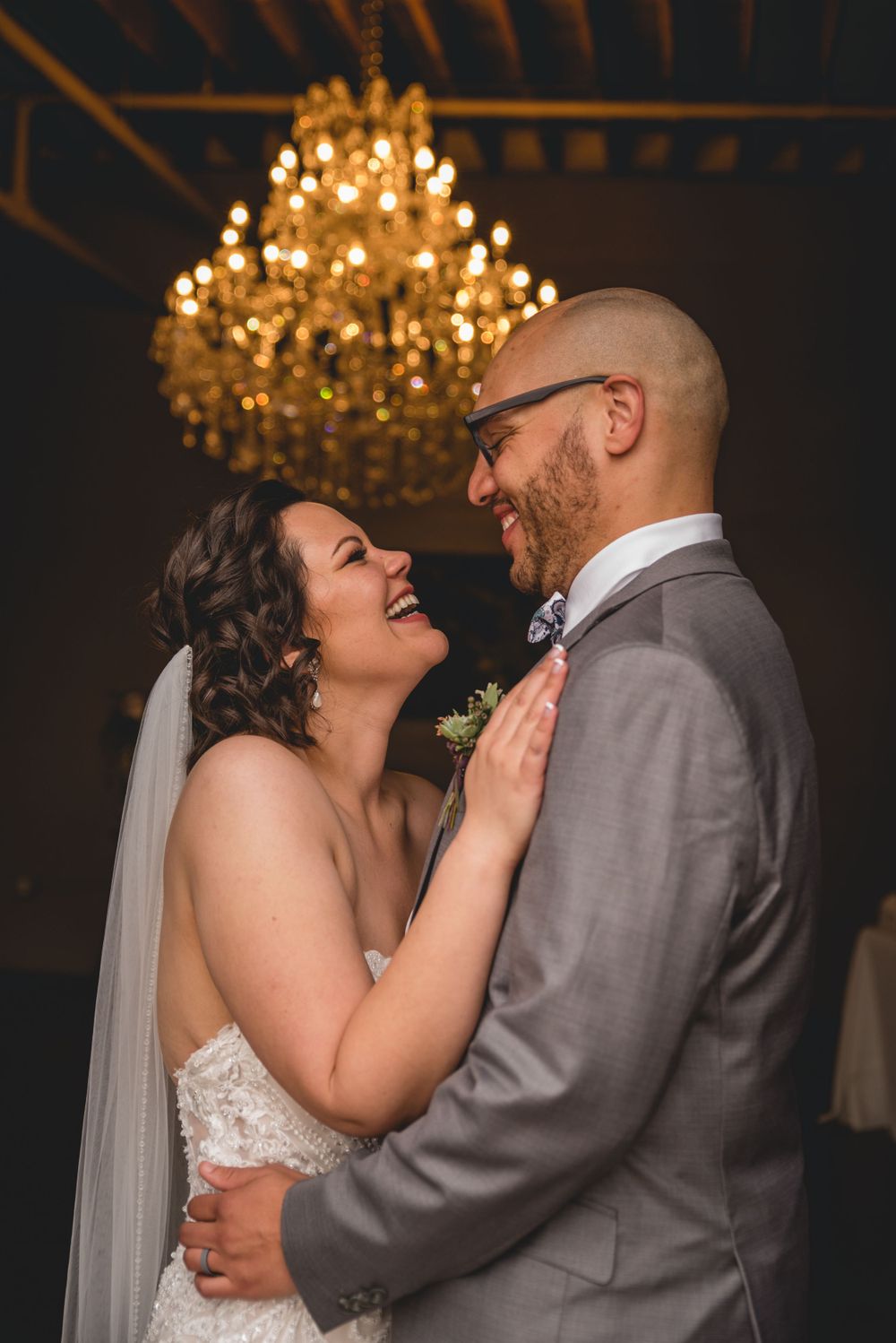 Happy newlyweds share an intimate moment under a grand chandelier during their wedding celebration.