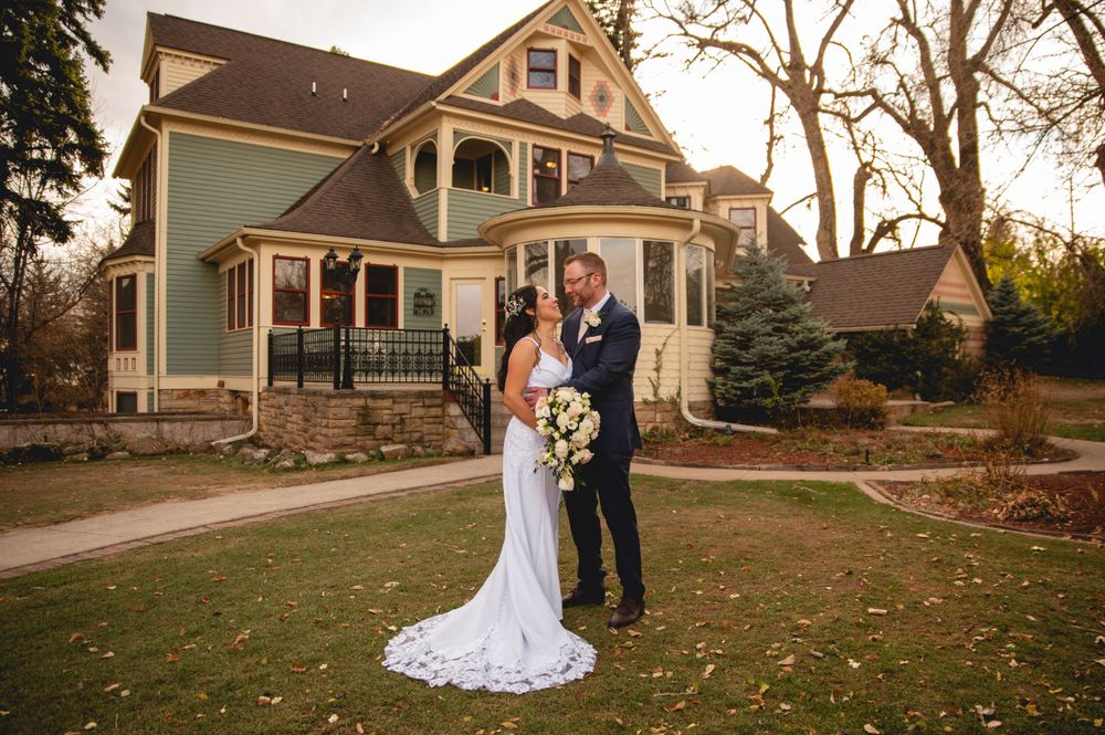 A wedding couple poses in front of a beautiful Victorian-style sage green Tapestry house at sunset