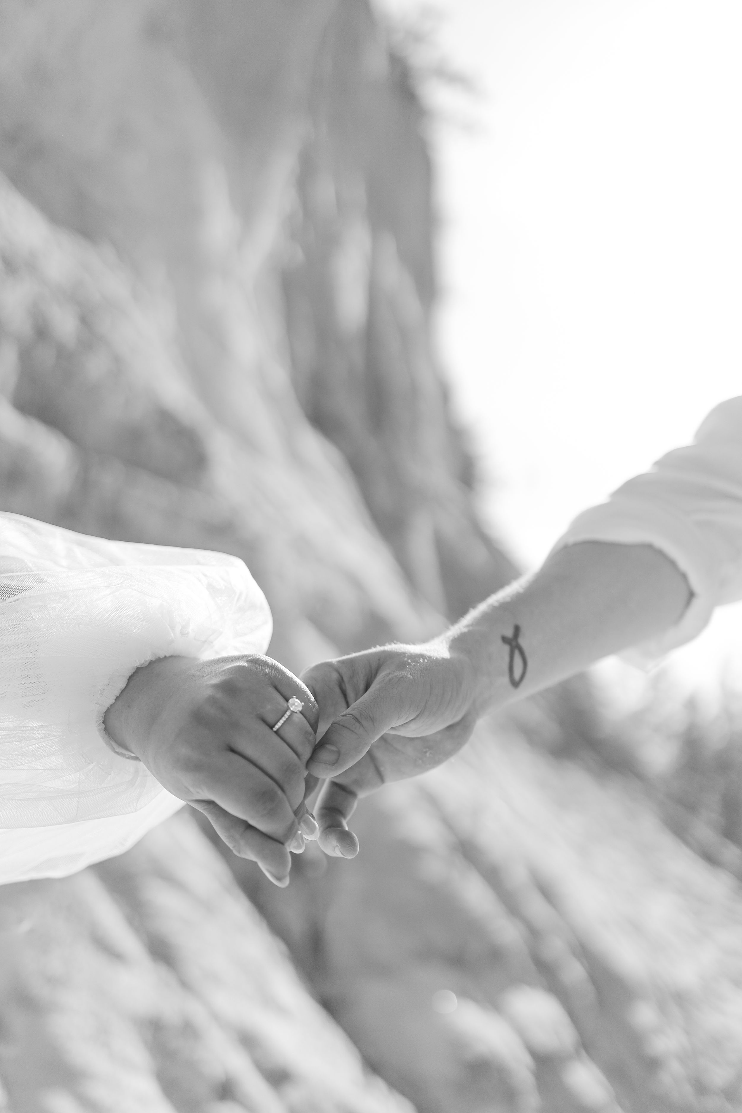 Black and white photo of two hands holding with an infinity symbol tattoo visible.