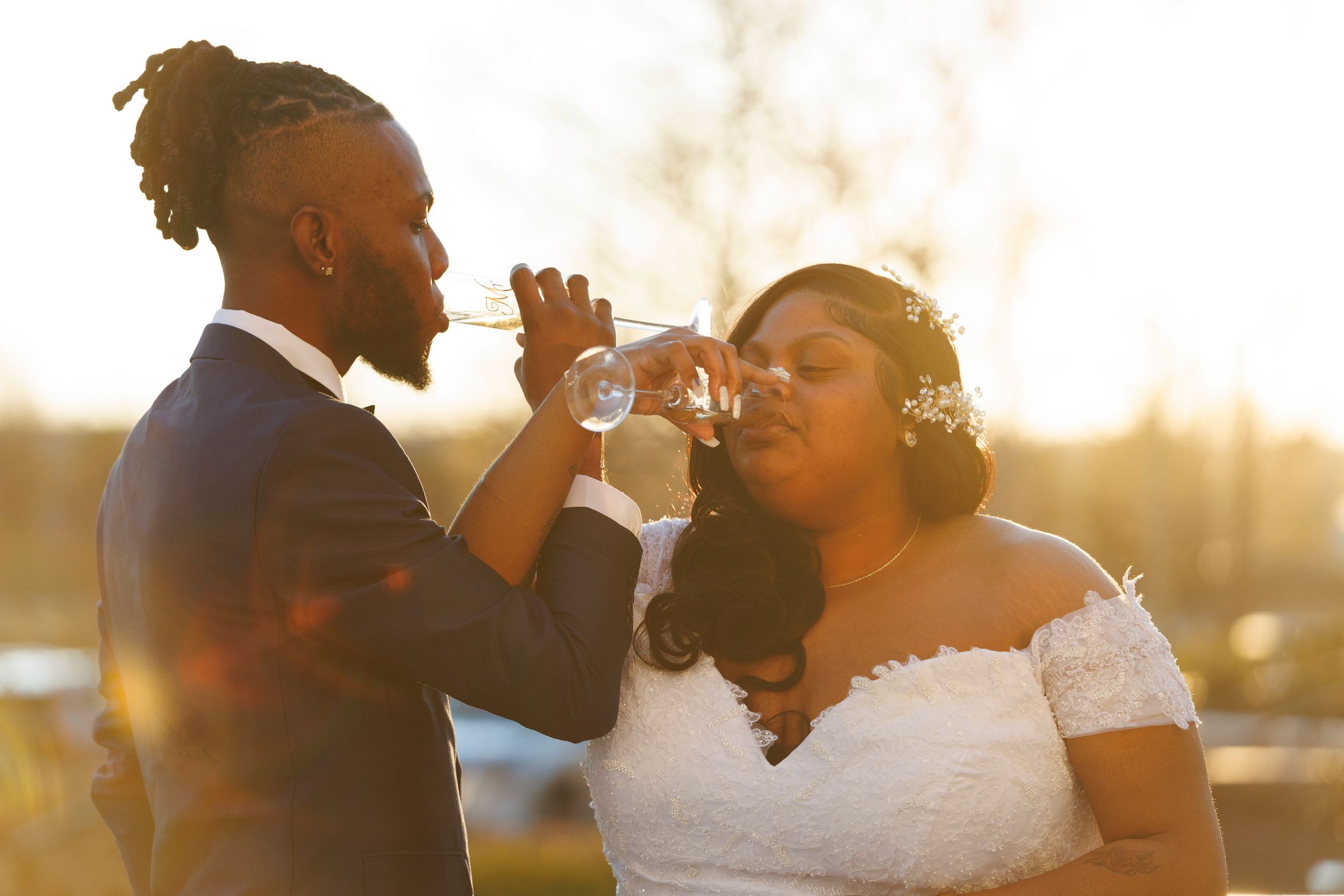 A couple in wedding attire shares a toast together at sunset during their outdoor wedding celebration.