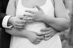 Black and white closeup of newlywed couple's hands embracing, showing wedding rings and formal attire.