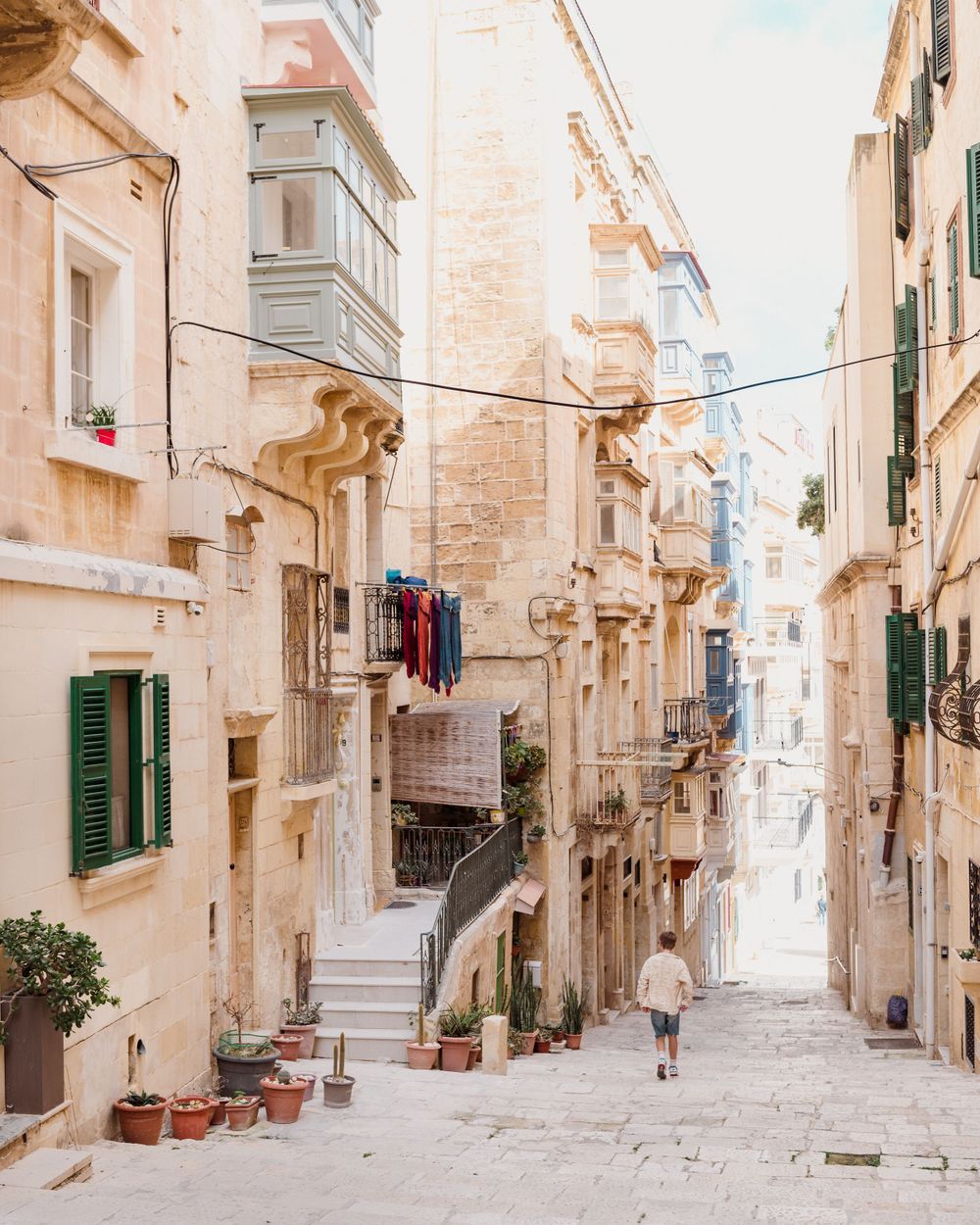 Narrow cobblestone street in Valletta, Malta with traditional limestone buildings and ornate balconies on a sunny day.