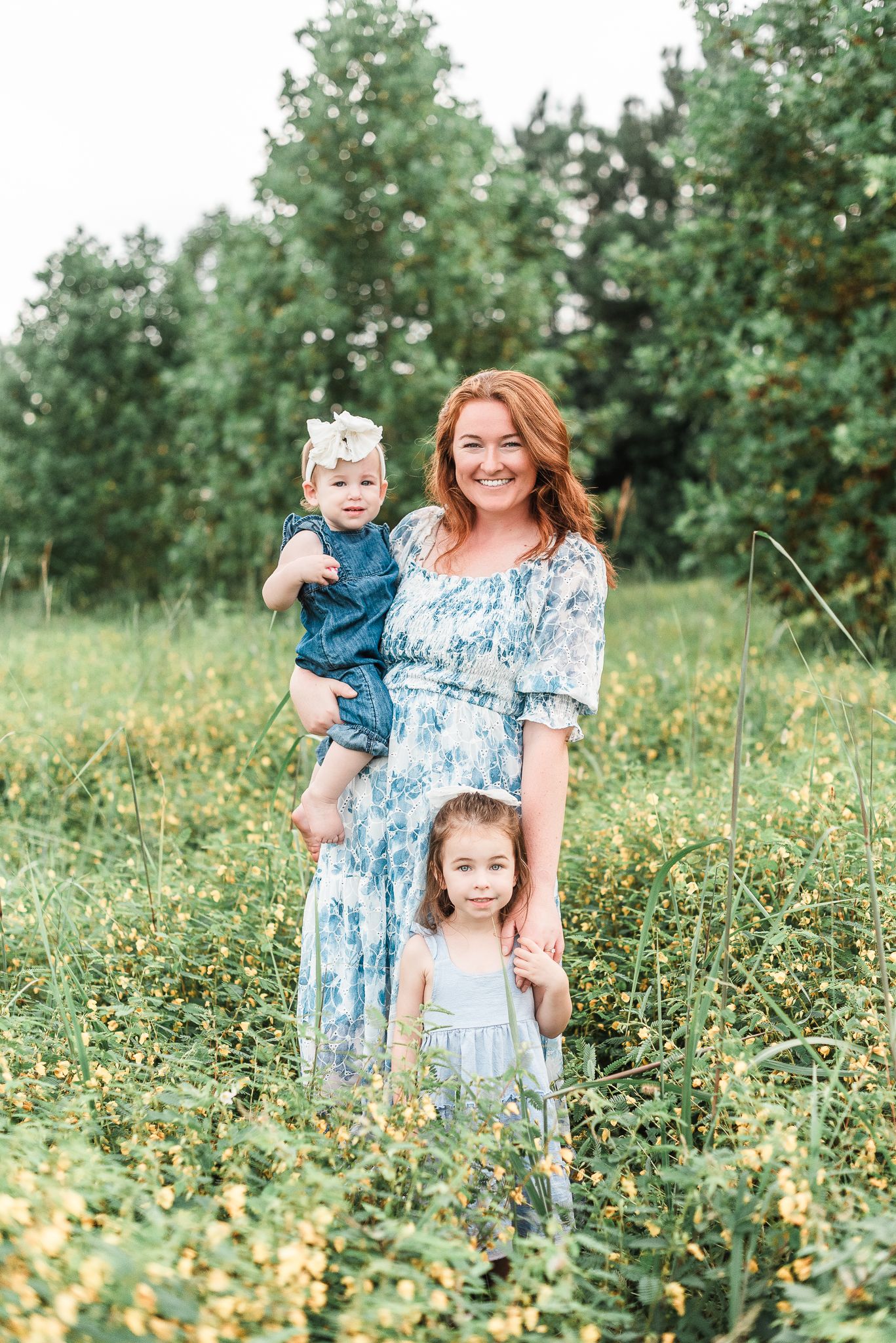 A mom and baby daughter in soft neutral tones embraces outdoors in a grassy field during a golden hour photoshoot.