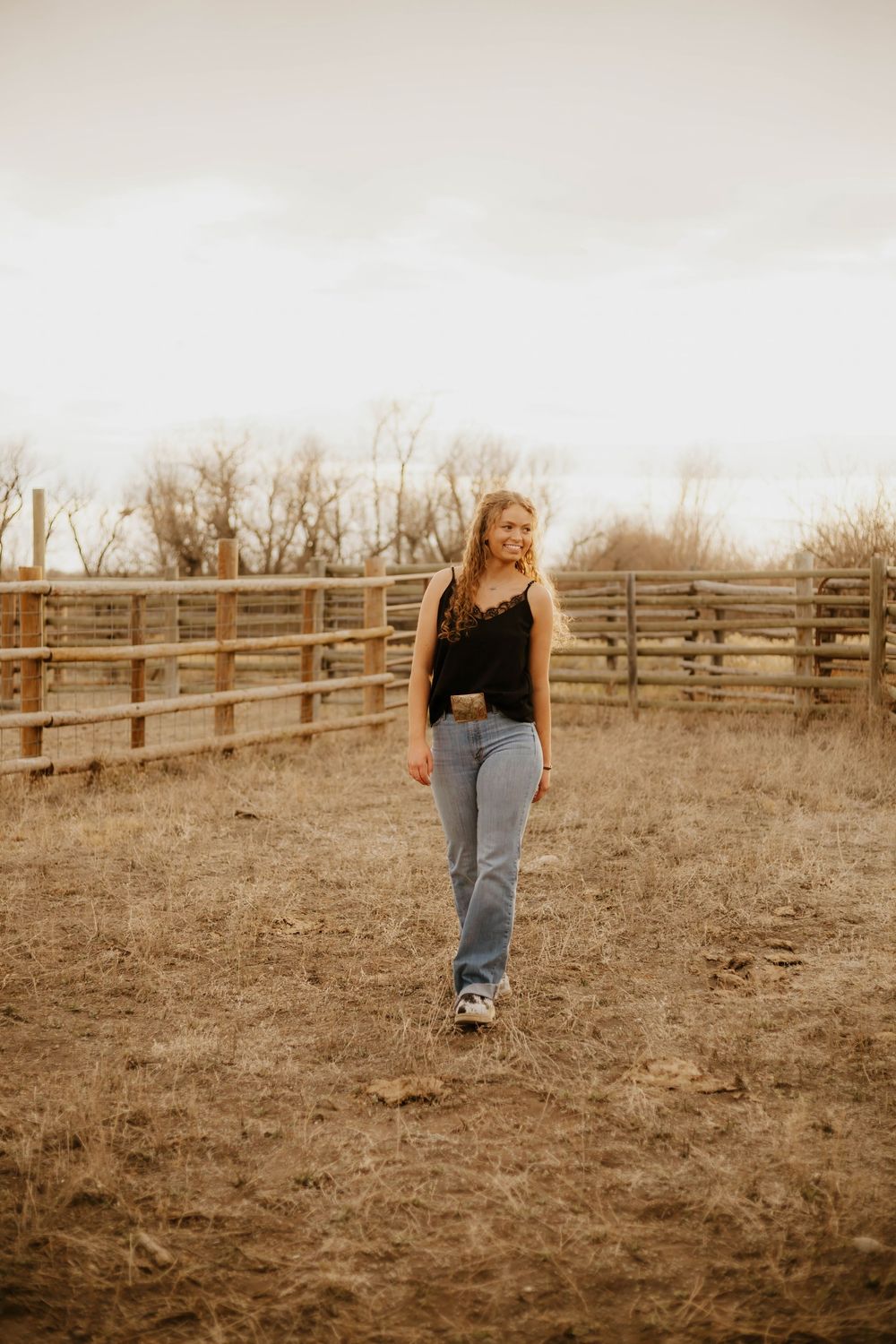 Western Walking shots in jeans and black top against rustic ranch fence background.