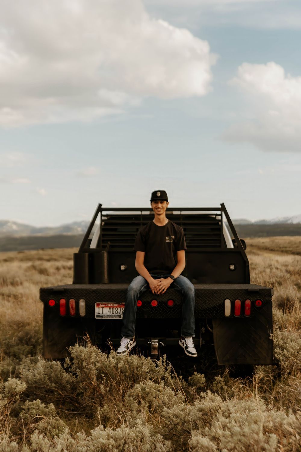 Casual western poses on black flatbed truck in desert landscape with mountains in background.