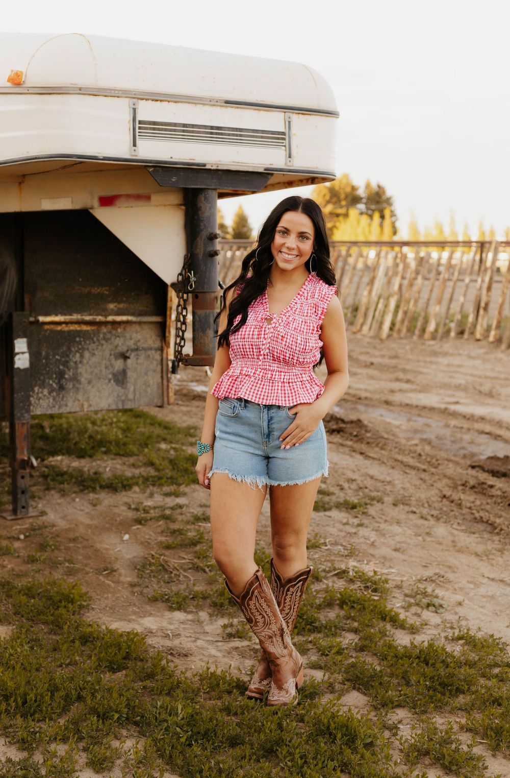 Country-style fashion with cowboy boots, denim shorts, and pink top photographed near a rustic barn.