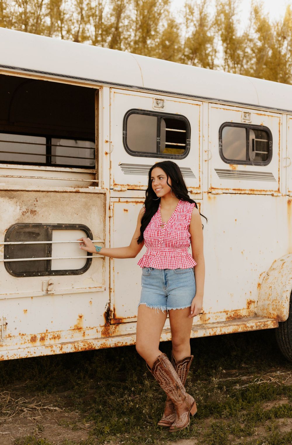 Western photoshoot featuring cowboy boots and casual attire against a white horse trailer backdrop.