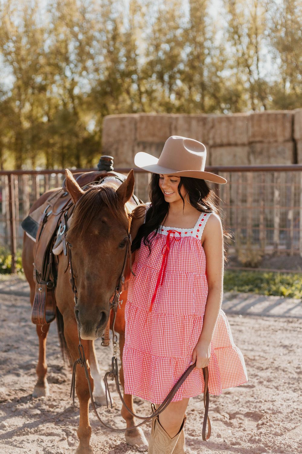 A pink gingham top and brown saddle displayed on a horse against a rustic wooden fence background.