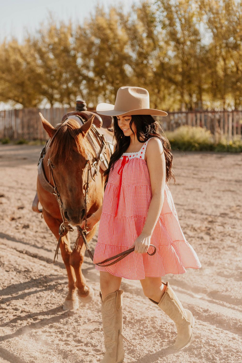 Western-style outfit with pink top and tan hat shown beside a saddled horse in a sunny outdoor setting.
