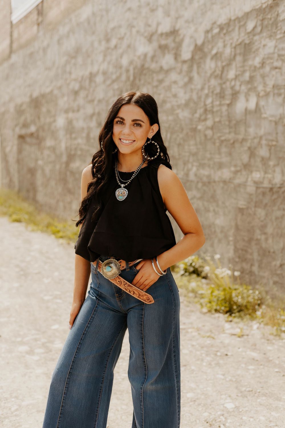 Casual western denim and black top ensemble photographed against a textured stone wall background.