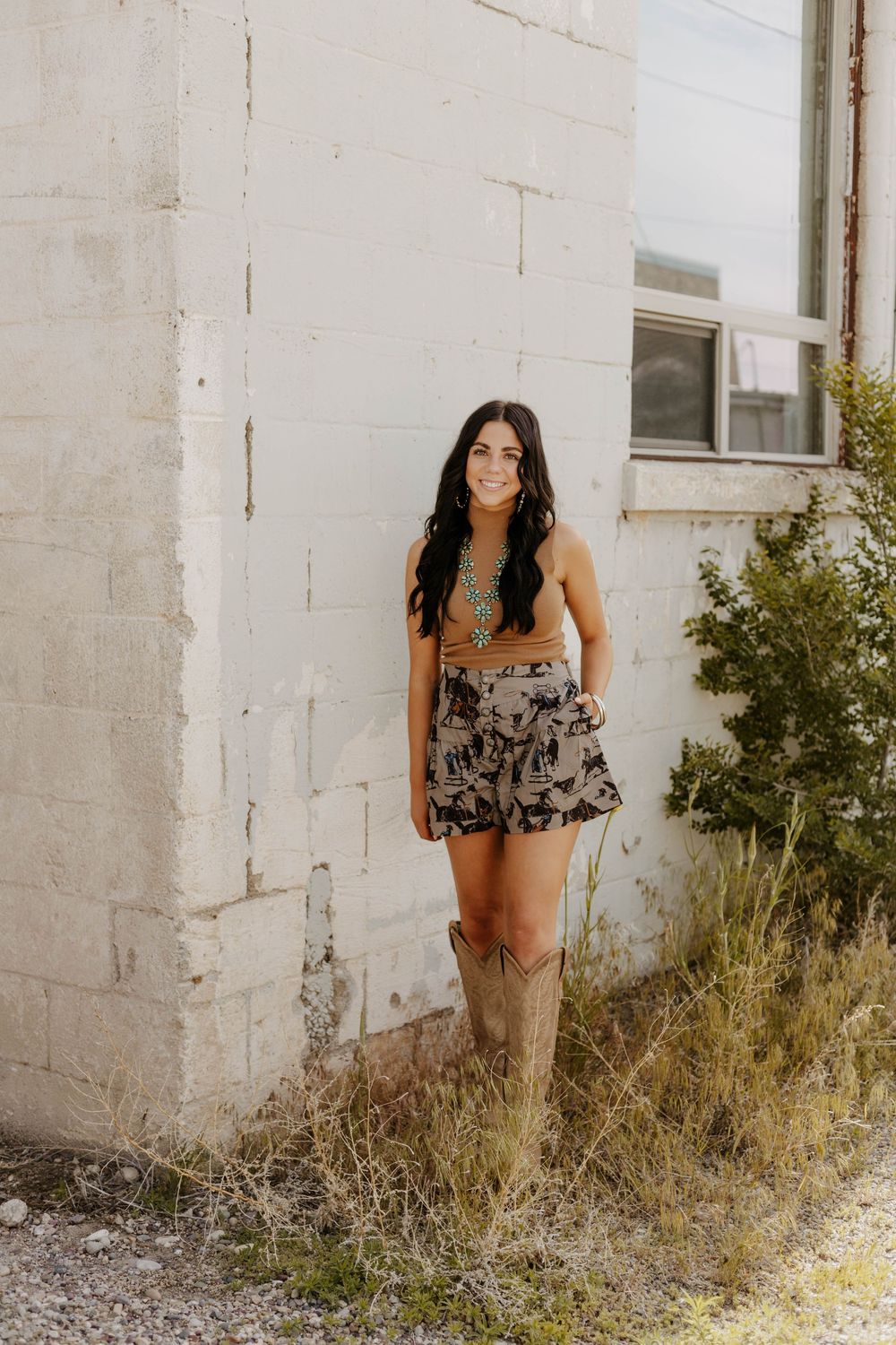 Western Summer fashion photographed against a white brick wall with natural greenery.