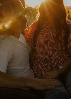 A western couple sit close together in his truck with sunlight streaming behind them in a warm romantic silhouette view.