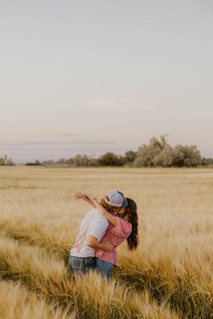 A western couple embraces romantically in a golden wheat field at sunset creating a serene countryside scene.