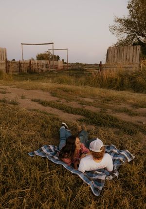 photos show western couple lying in a grassy field at sunset on family land and near the farm buildings in the background.