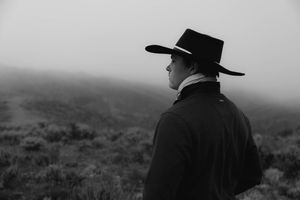 Black and white photo of a man in a cowboy hat gazing into a misty, foggy landscape from behind.
