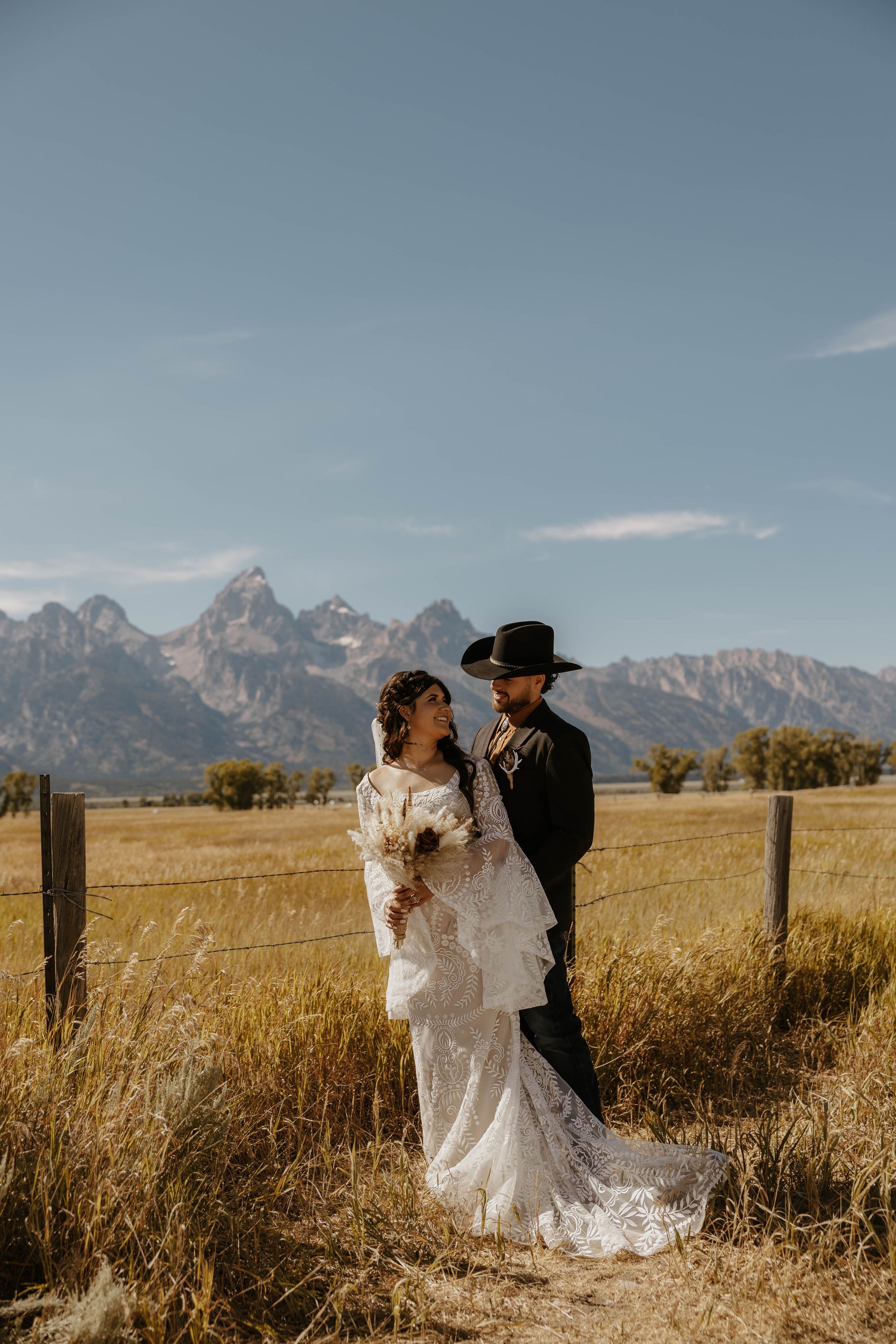 A wedding couple embraces in front of majestic mountain peaks and fence posts. Located in The Grand Teton National Park