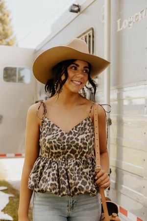 A leopard print top and wide-brimmed hat styled against a horse trailer. This western girl is ready for the rodeo!