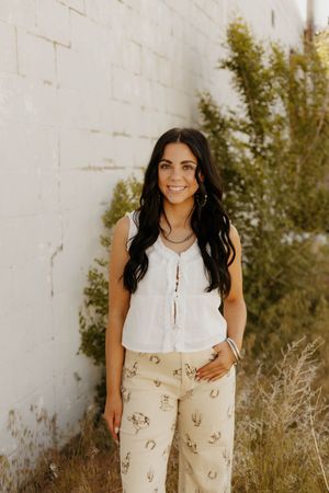 A western white ruffled sleeveless top paired with beige printed pants in an outdoor setting.