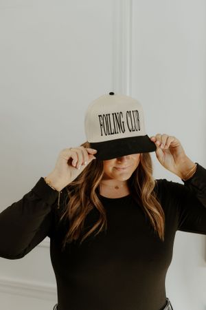 Person in black wearing a 'Fooling Club' baseball cap adjusting the brim.