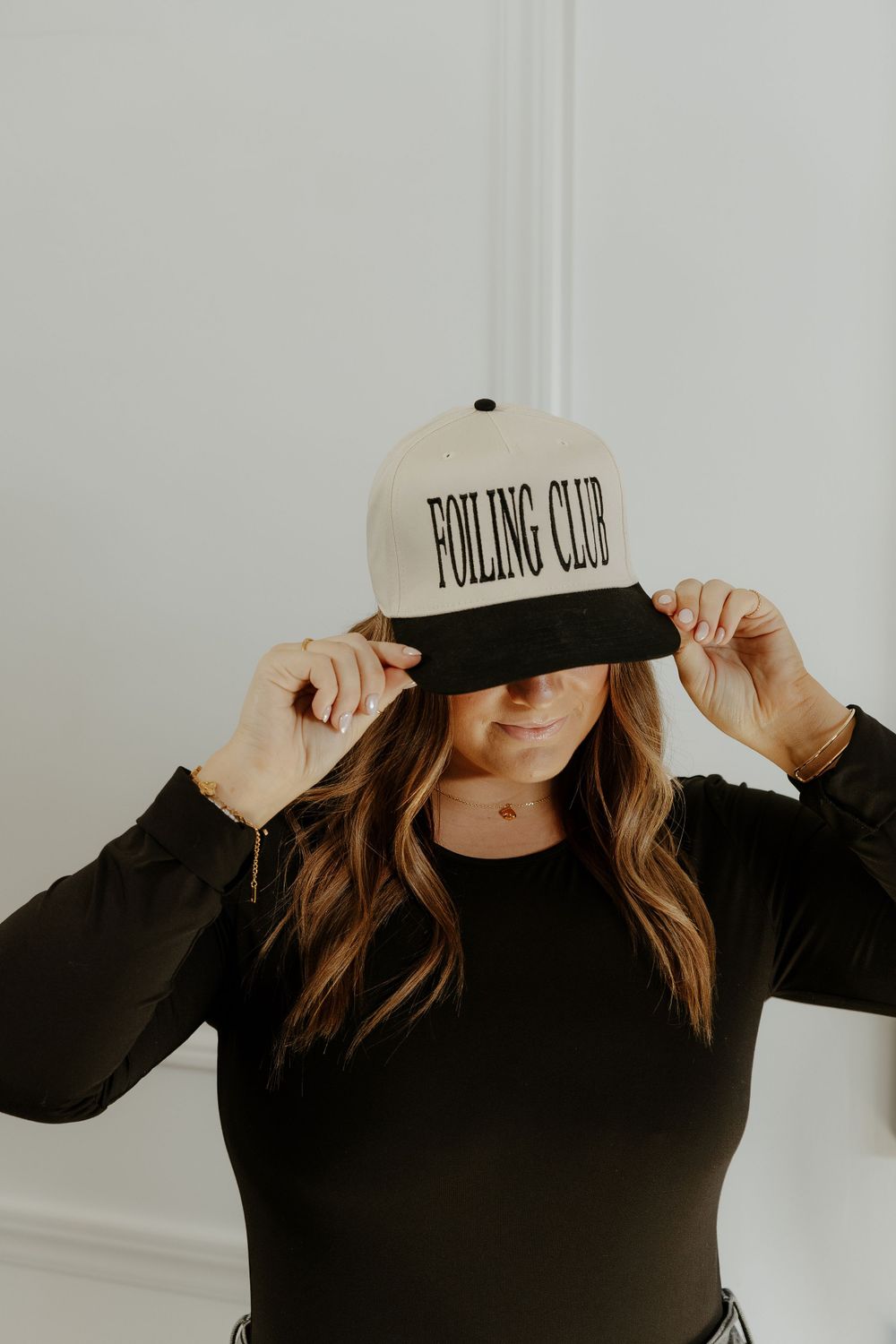 Person in black wearing a 'Fooling Club' baseball cap adjusting the brim.