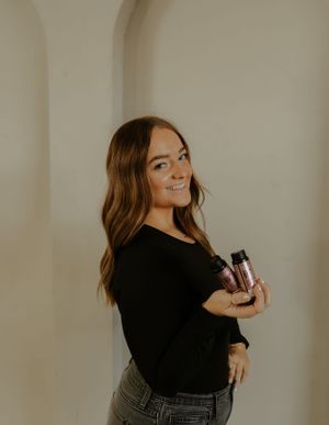 Woman in black top posing against white wall with warm lighting.