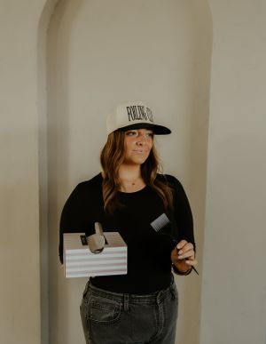 Person in black outfit holding products while wearing a 'Foiling Club' baseball cap.