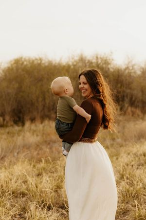 A western momma in a white dress spins joyfully with her baby in an autumn field.
