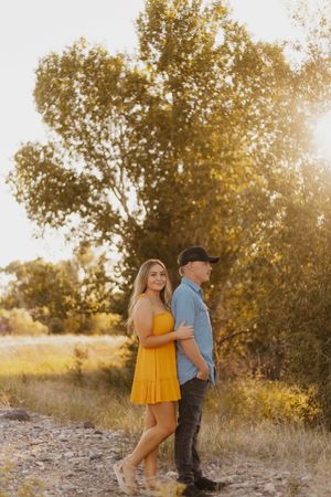 A western couple embraces in golden sunlight with autumn trees behind them.