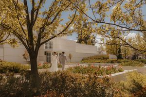 Couple walking through a garden with colorful tulips and autumn trees beside a white building.