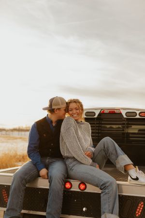 Western Couple sharing an intimate moment while sitting on the back of a pickup truck at sunset.