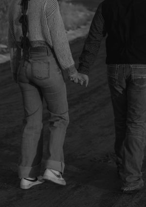 Black and white close-up of two people holding hands while walking together.